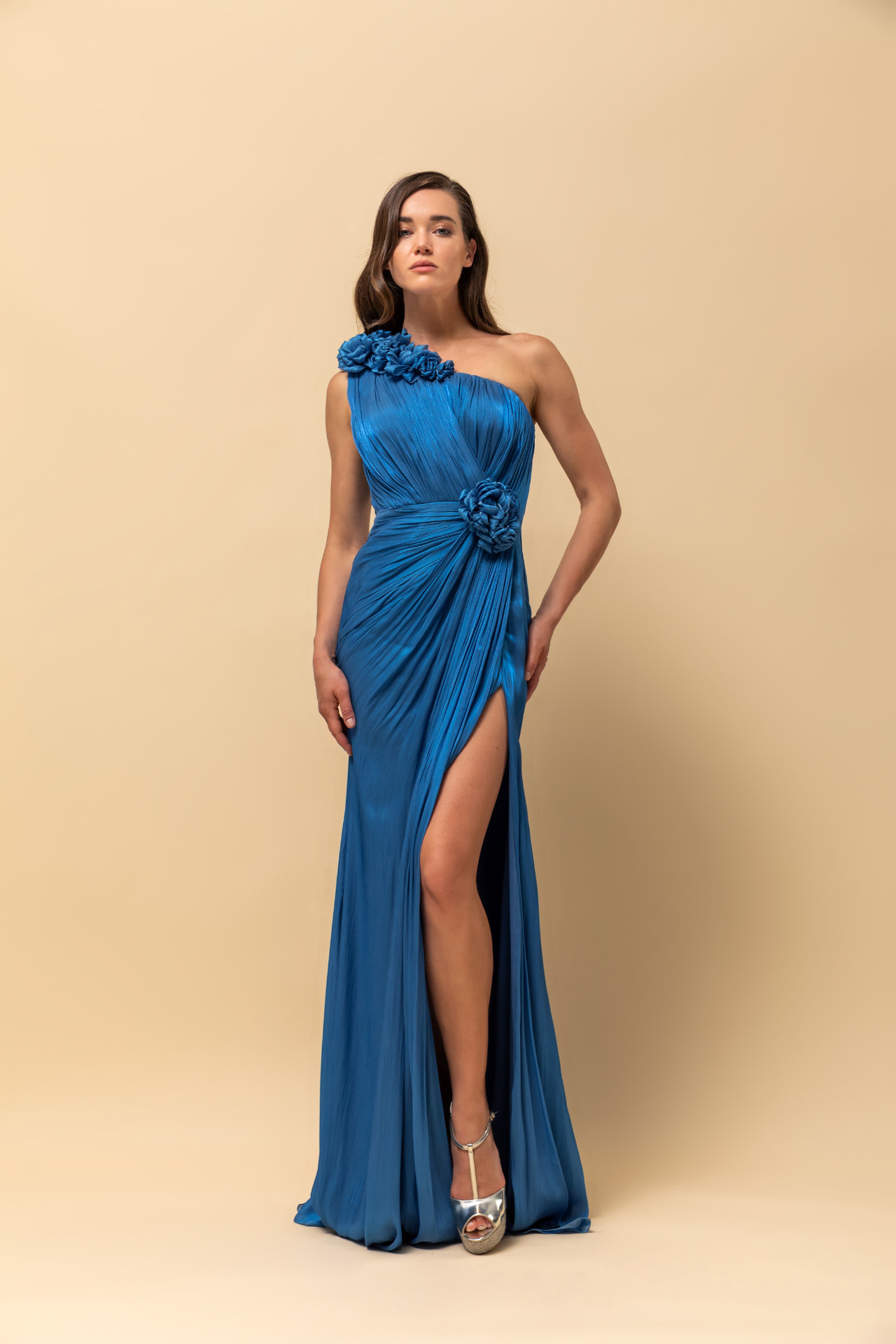 Blue pleated silk one-shoulder gown with rosette details and high slit