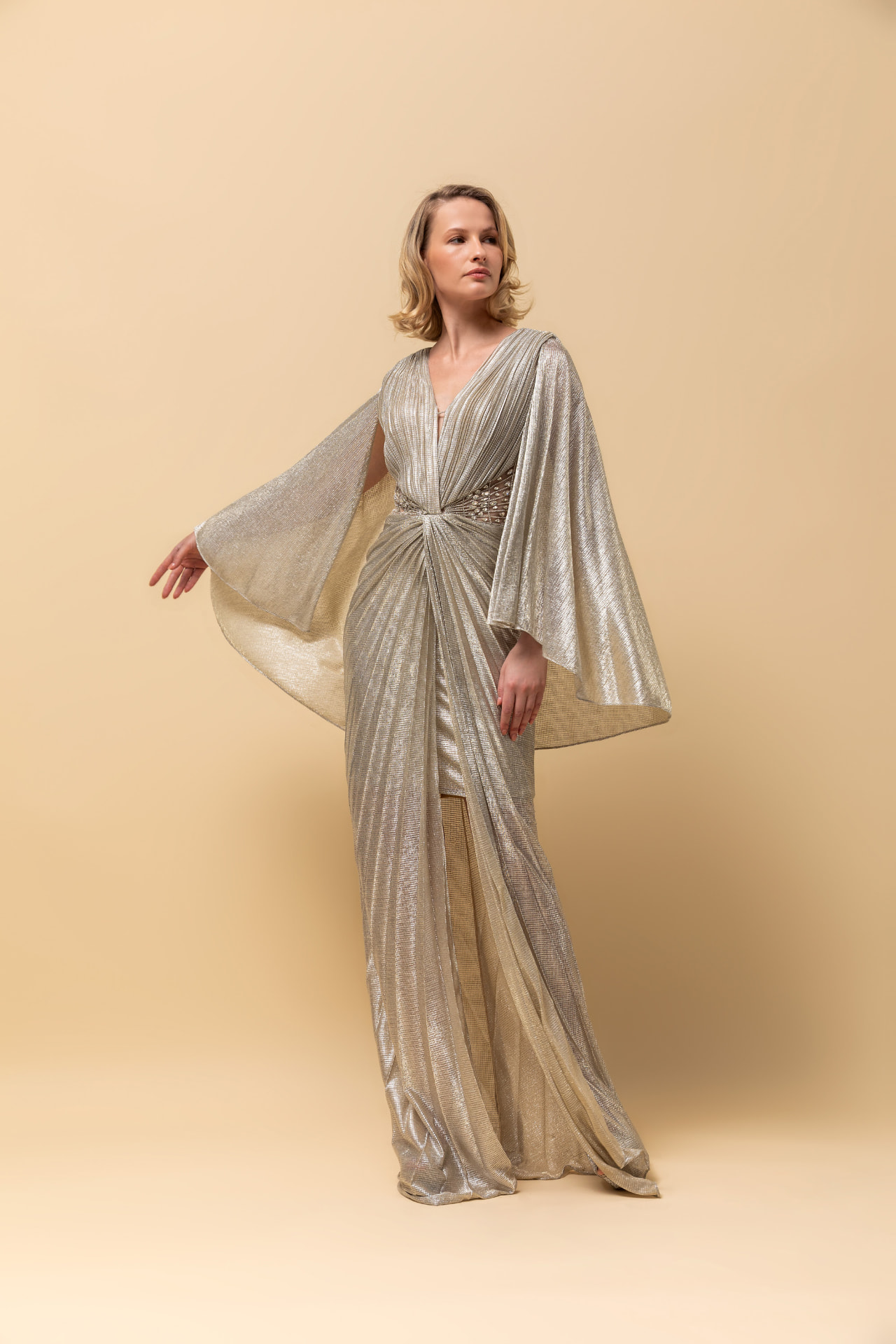 Champagne metallic pleated gown with dramatic cape sleeves and beaded waist