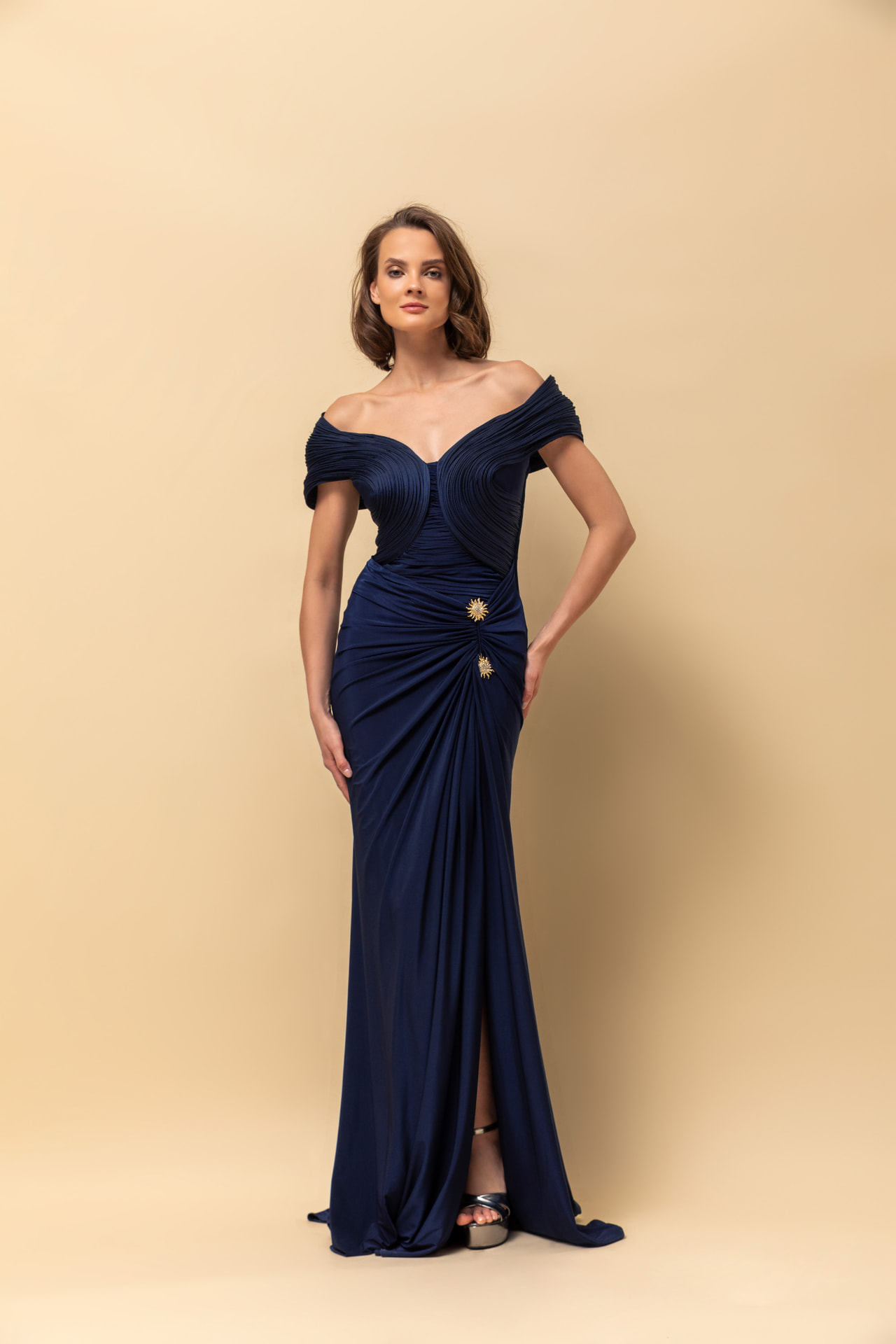 Navy off-shoulder jersey gown with gold sunburst brooches and high slit